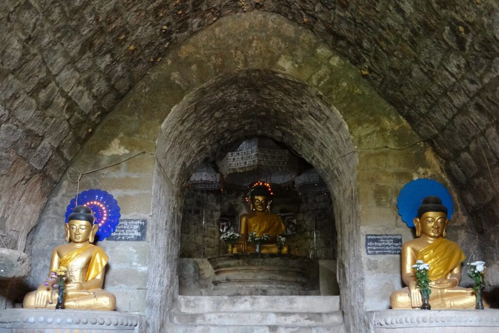 Interior de templos em Mrauk U decorado com três imagens de Buda, templo com acabamento em pedras e formato oval em direção ao teto