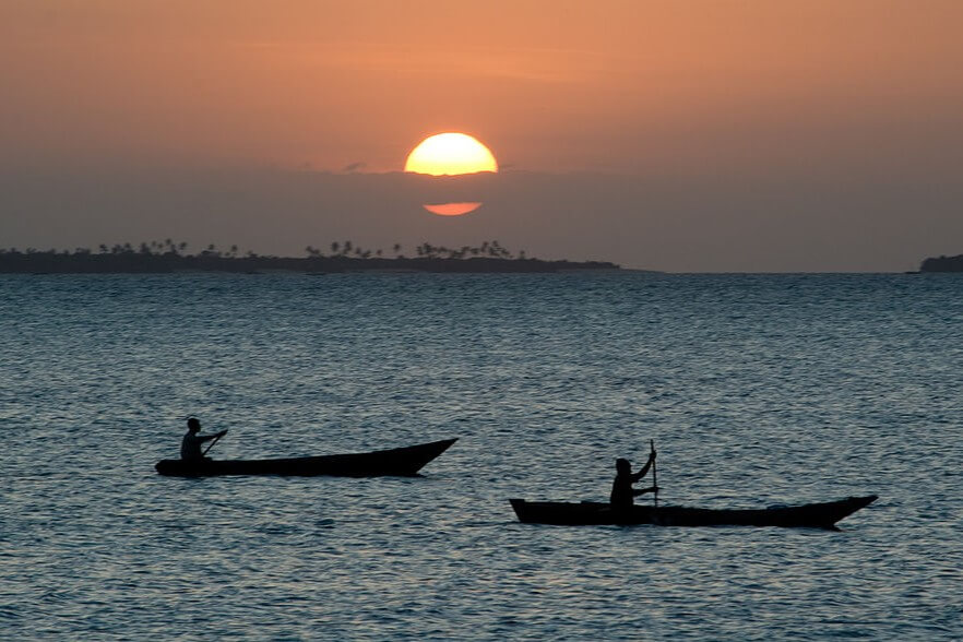 Duas pessoas navegando em dois respectivos Dhows, no contra luz, no fim de tarde em Zanzibar, um dos 20 melhores destinos para viajar em 2025.